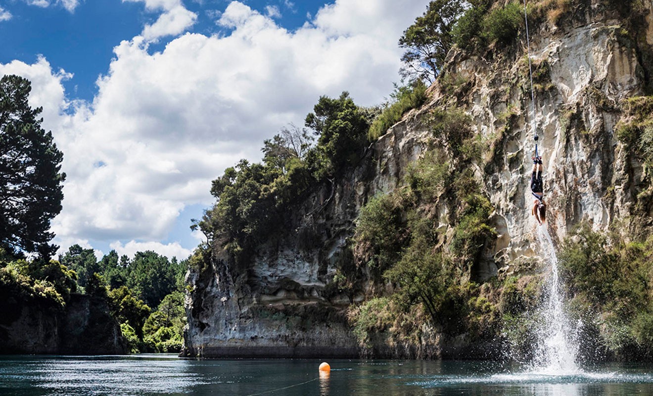 Person mid-air bungy jumping into calm water below at AJ Hackett Bungy in Taupō, New Zealand.